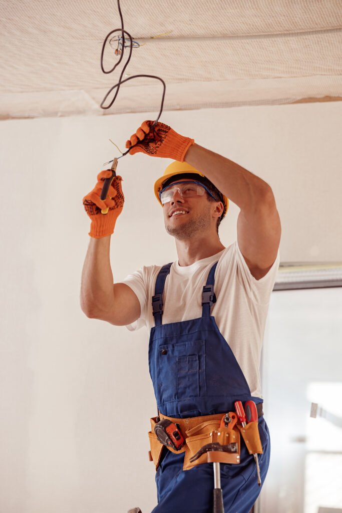 Cheerful electrician repairing electric cable on ceiling